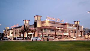 Aswaaq shopping center exterior illuminated at dusk with front lawn and parking, KhaleejFusion