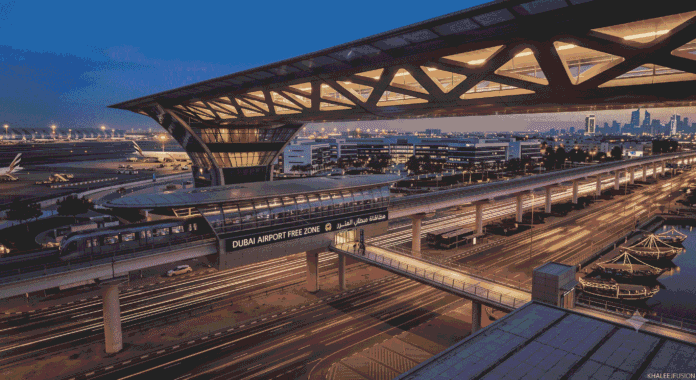 An aerial dusk view of the Dubai Airport Free Zone Metro Station and tracks, with blurred traffic light trails and the text 