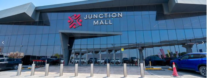 Exterior view of Junction Mall featuring a modern dark-tinted glass facade, entrance canopy, and front parking lot, KhaleejFusion