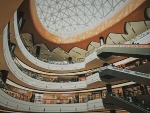 Indoor multi-story shopping mall atrium with escalators and a glass skylight ceiling, KhaleejFusion