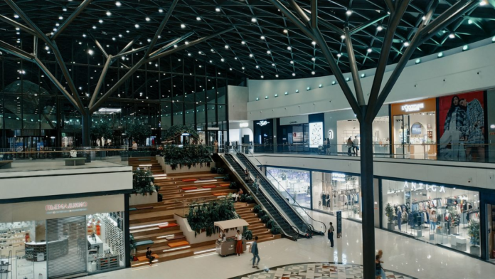Indoor mall atrium with tiered seating steps, escalators, and retail stores, KhaleejFusion