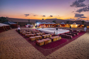 Traditional Bedouin-style desert camp setup in Dubai featuring low seating, rugs, and tents at sunset, Khaleej Fusion