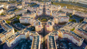 Aerial view of Dubai International City showcasing the unique radial cluster layout of residential buildings and parking areas, Khaleej Fusion
