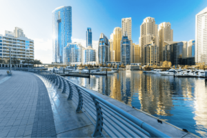 Scenic view of the Dubai Marina waterfront promenade, docked yachts, and towering skyscrapers under a clear blue sky, Khaleej Fusion